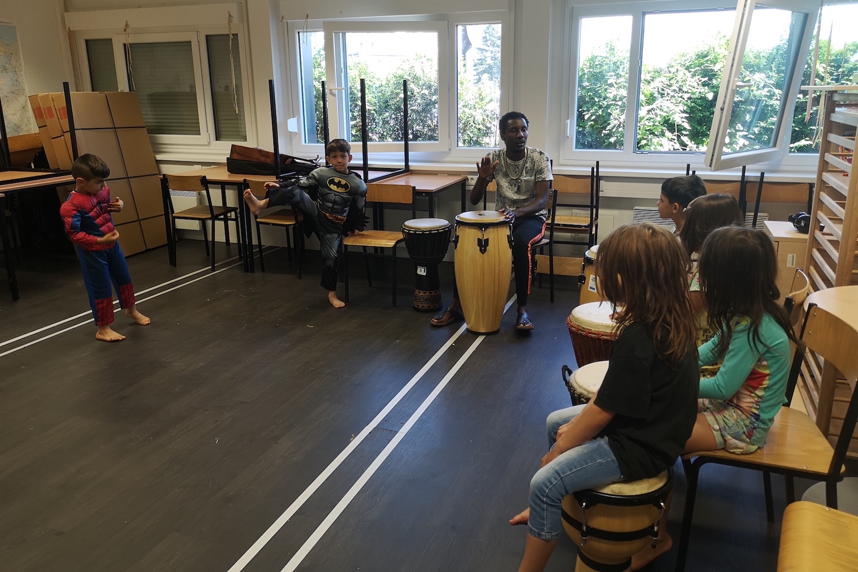 Kinder spielen mit Dozent auf Djemben und Congas, 2 Kinder stehen verkleidet und beobachtend dabei